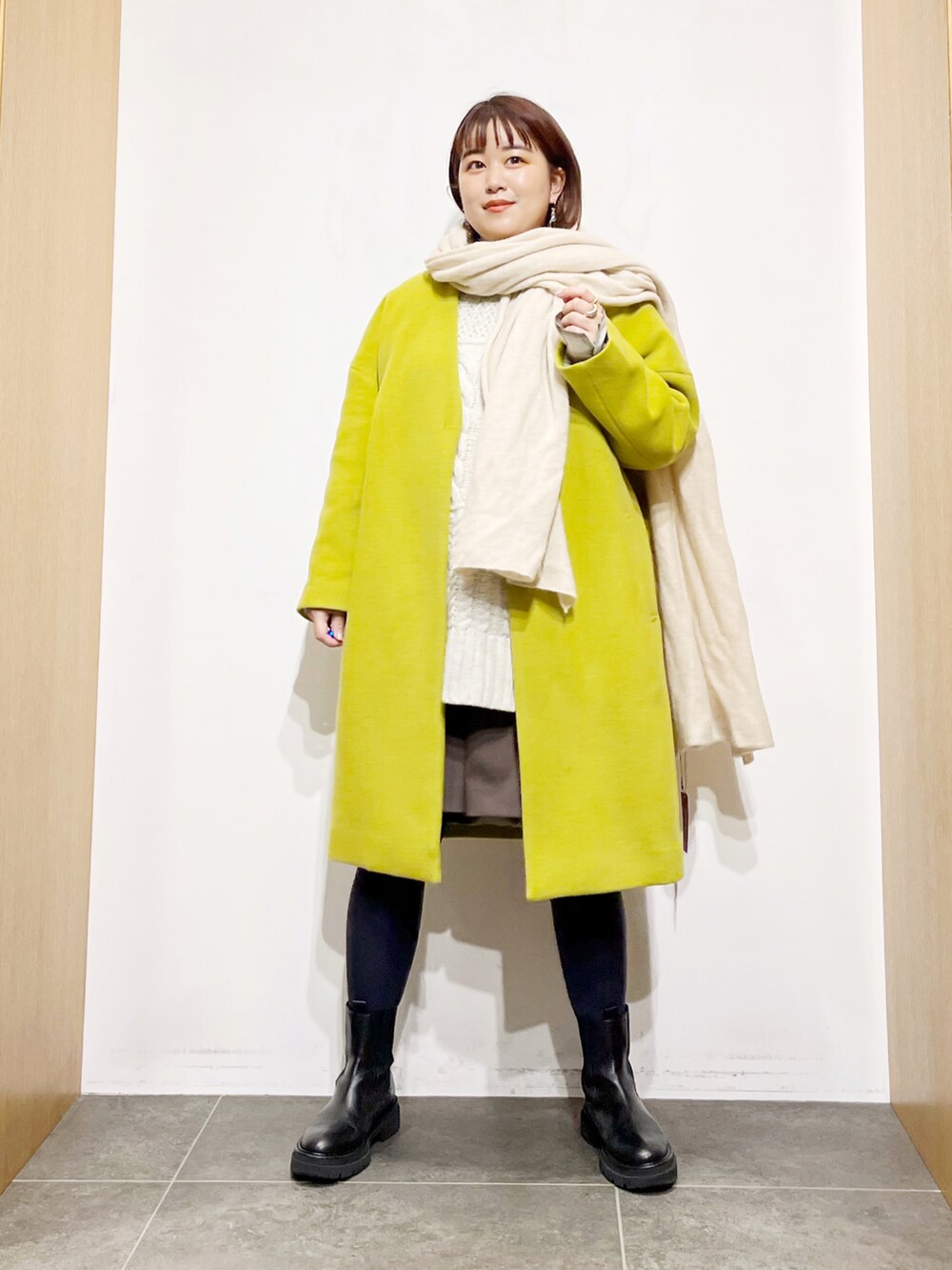 イエロー系のその他アウター、ホワイト系のニット/セーター、ブラック系のブーツを着用したレディースの冬コーディネートの2枚目の写真