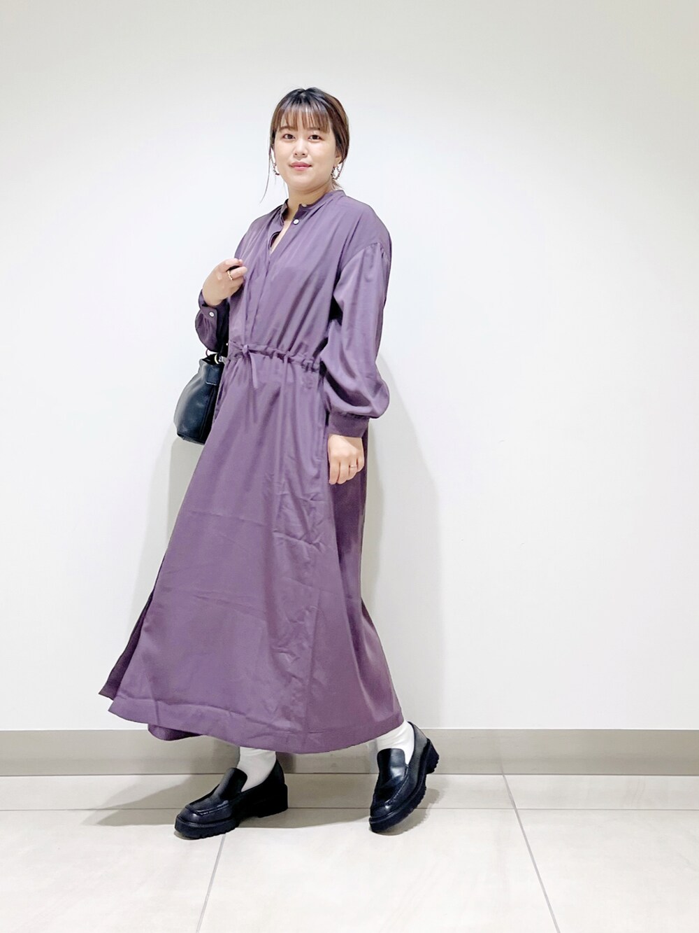 パープル系のワンピース、ブラック系のローファー、ブラック系のハンドバッグを着用したレディースの秋コーディネートの5枚目の写真