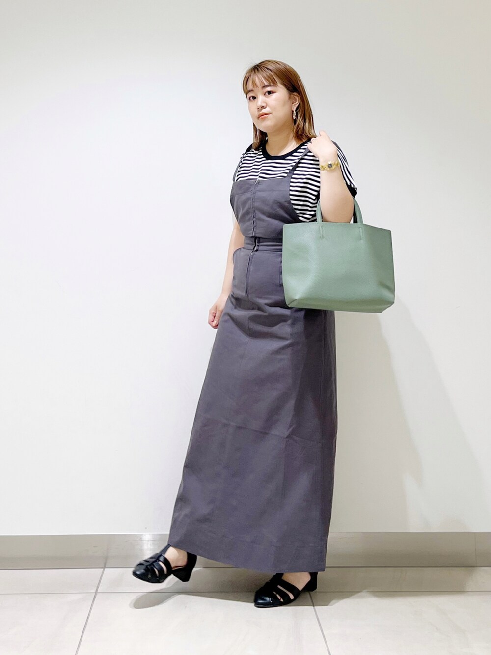 グレー系のワンピース、グリーン系のトートバッグ、ブラック系のサンダルを着用したレディースの春コーディネートの3枚目の写真