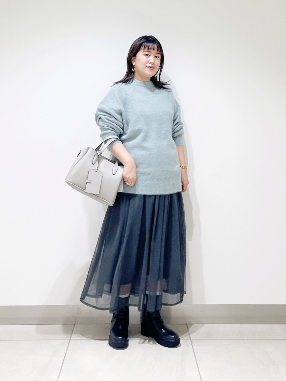 グリーン系のニット/セーター、グレー系のスカート、グレー系のトートバッグを着用したレディースの秋コーディネートの3枚目の写真