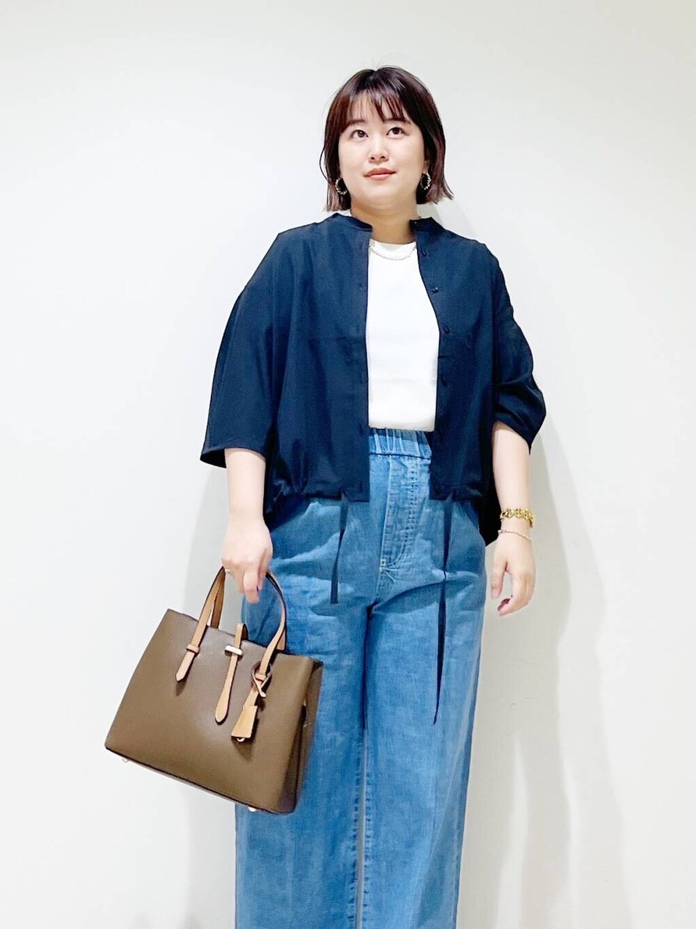 ブラウン系のトートバッグ、ブルー系のデニムパンツ、ブラック系のサンダルを着用したレディースの春コーディネートの3枚目の写真