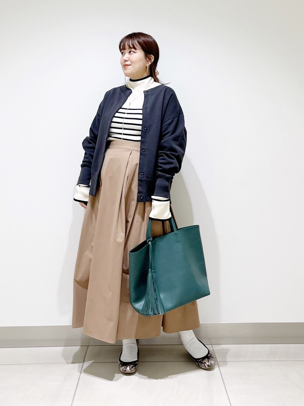 グリーン系のトートバッグ、ベージュ系のスカート、その他のバレエシューズを着用したレディースの秋コーディネートの5枚目の写真