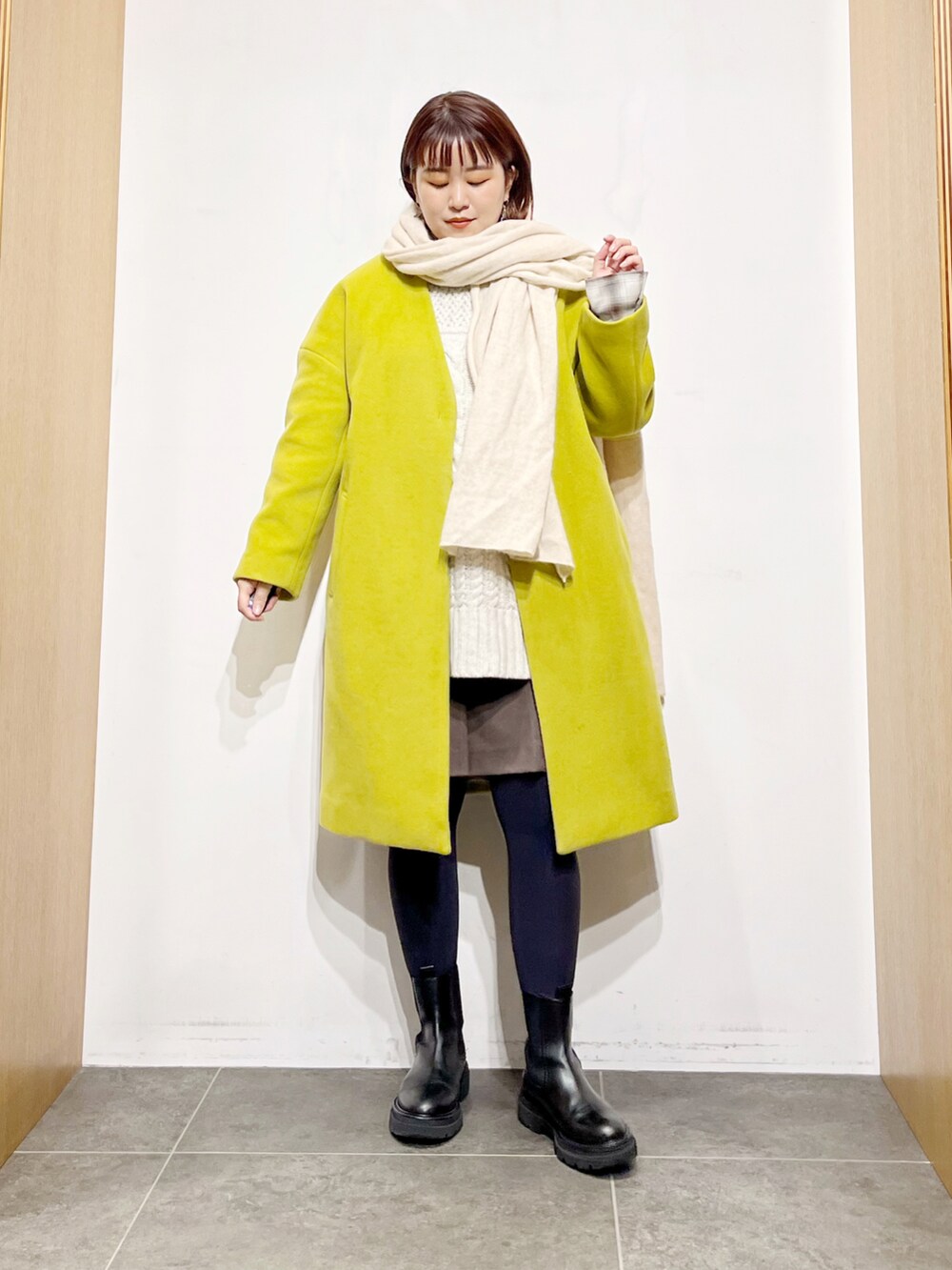 イエロー系のその他アウター、ホワイト系のニット/セーター、ブラック系のブーツを着用したレディースの冬コーディネートの4枚目の写真