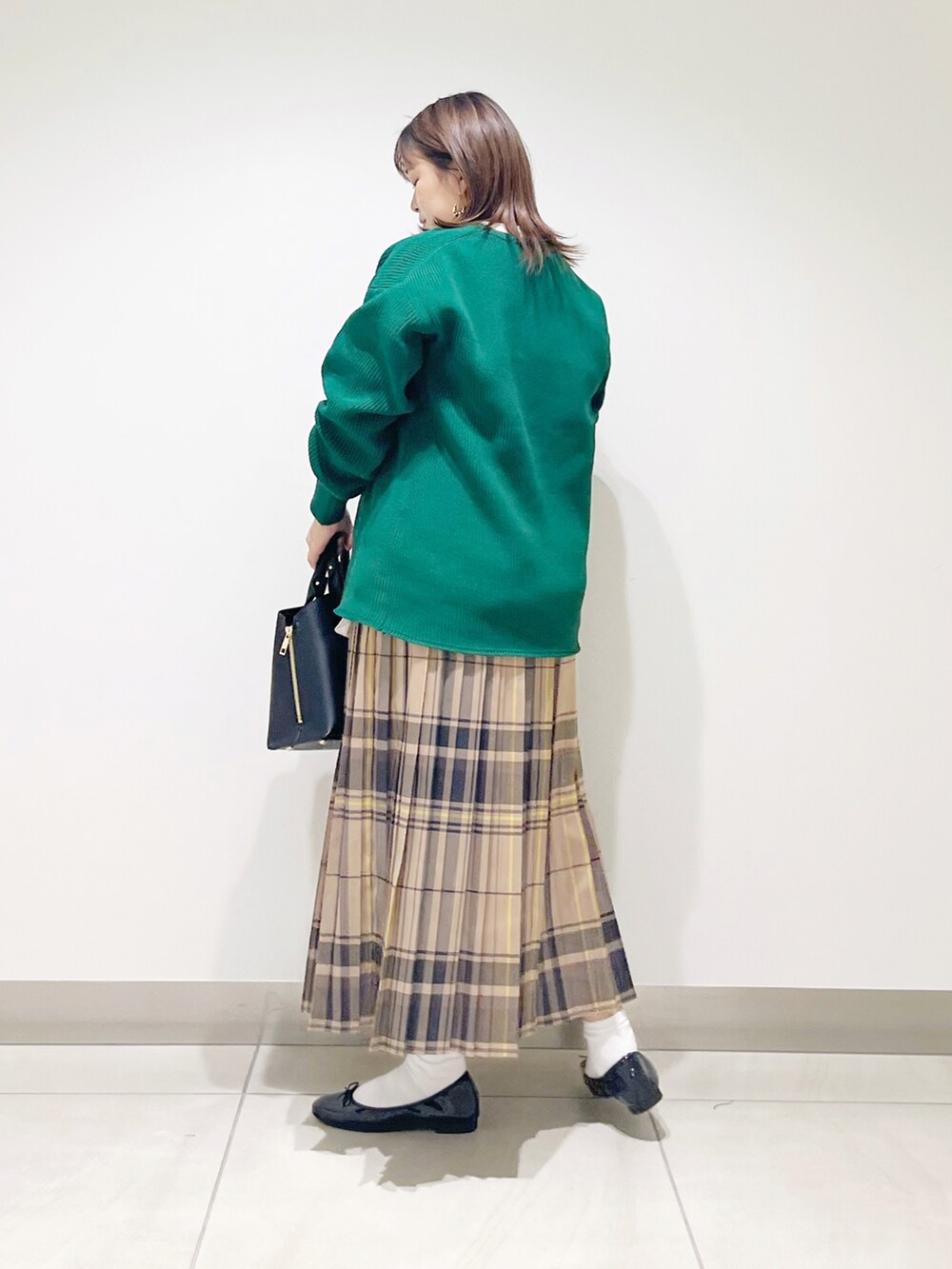 グリーン系のニット/セーター、ブラック系のトートバッグ、ベージュ系のスカートを着用したレディースの秋コーディネートの3枚目の写真