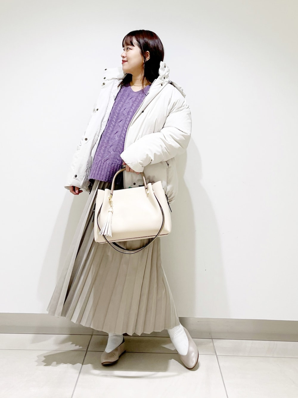 ホワイト系のダウンジャケット/コート、パープル系のニット/セーター、ベージュ系のスカートを着用したレディースの冬コーディネートの2枚目の写真