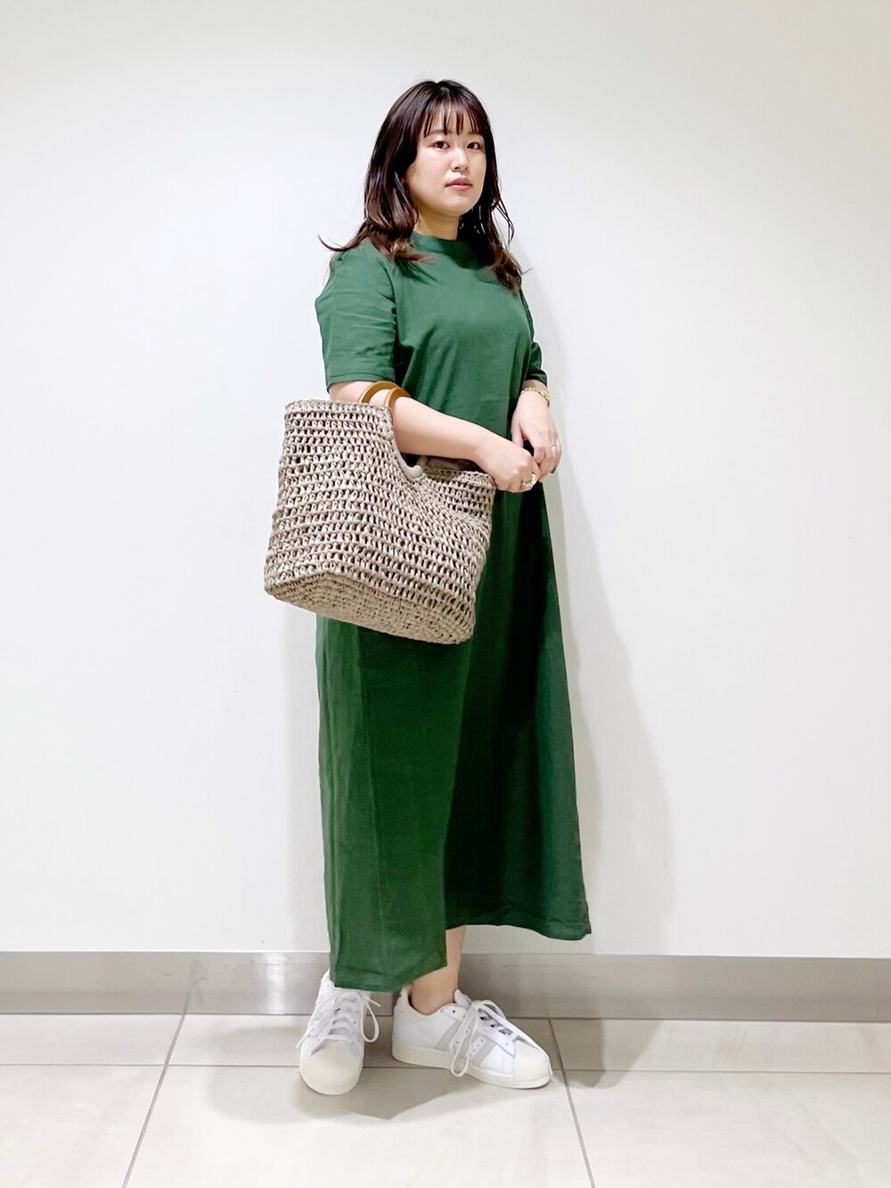 グリーン系のワンピース、グレー系のかごバッグ、ホワイト系のスニーカーを着用したレディースの夏コーディネートの2枚目の写真