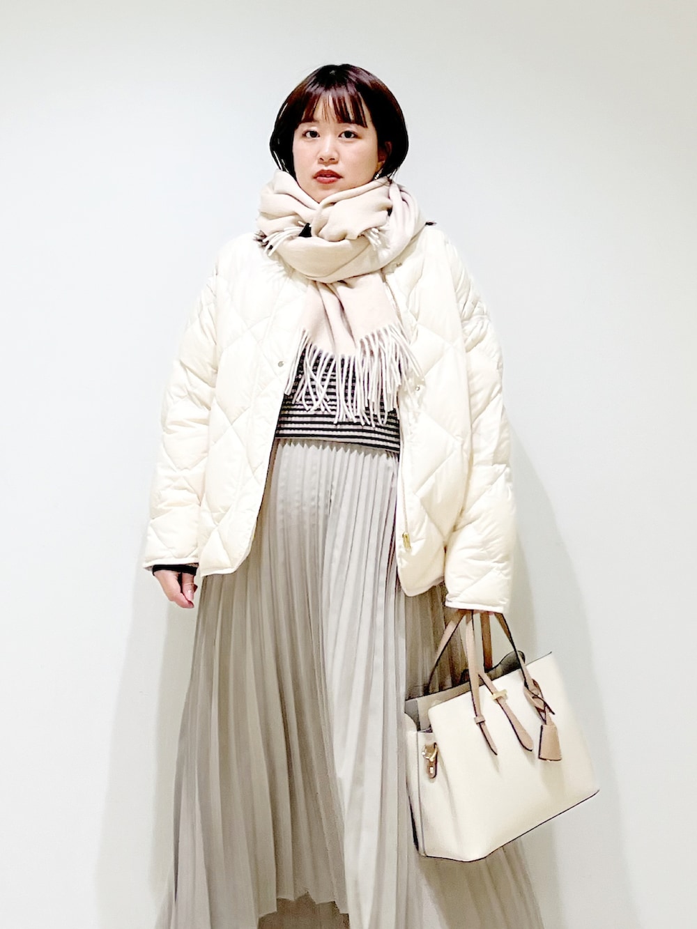 ホワイト系のダウンジャケット/コート、グレー系のニット/セーター、ベージュ系のスカートを着用したレディースの冬コーディネートの4枚目の写真