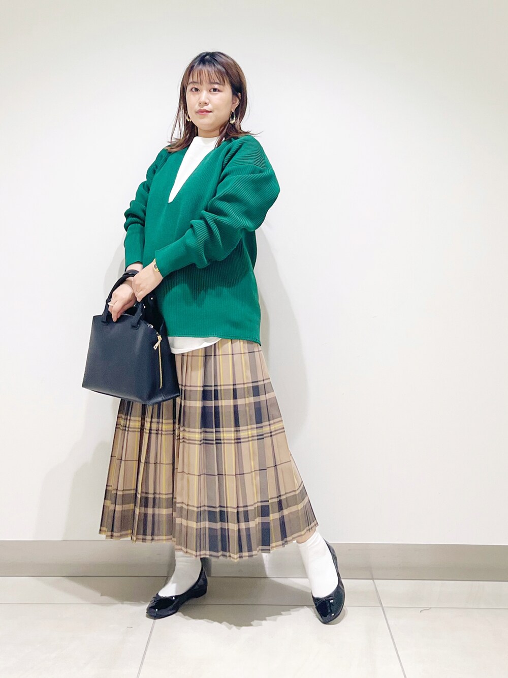 グリーン系のニット/セーター、ブラック系のトートバッグ、ベージュ系のスカートを着用したレディースの秋コーディネートの5枚目の写真