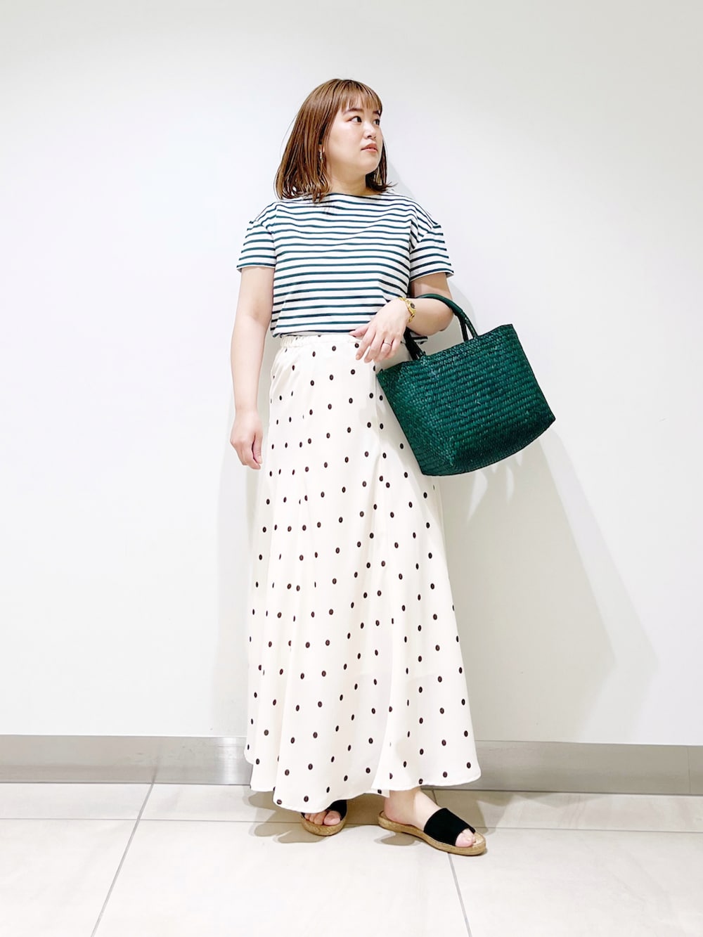 ホワイト系のスカート、グリーン系のかごバッグ、グリーン系のTシャツ/カットソーを着用したレディースの春コーディネートの3枚目の写真