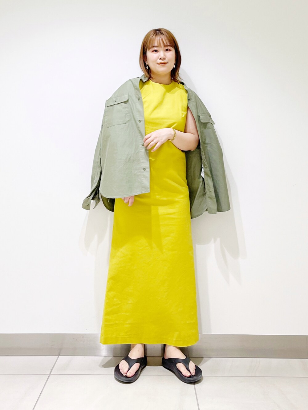 イエロー系のワンピース、グリーン系のシャツ/ブラウス、ブラック系のサンダルを着用したレディースの春コーディネートの2枚目の写真