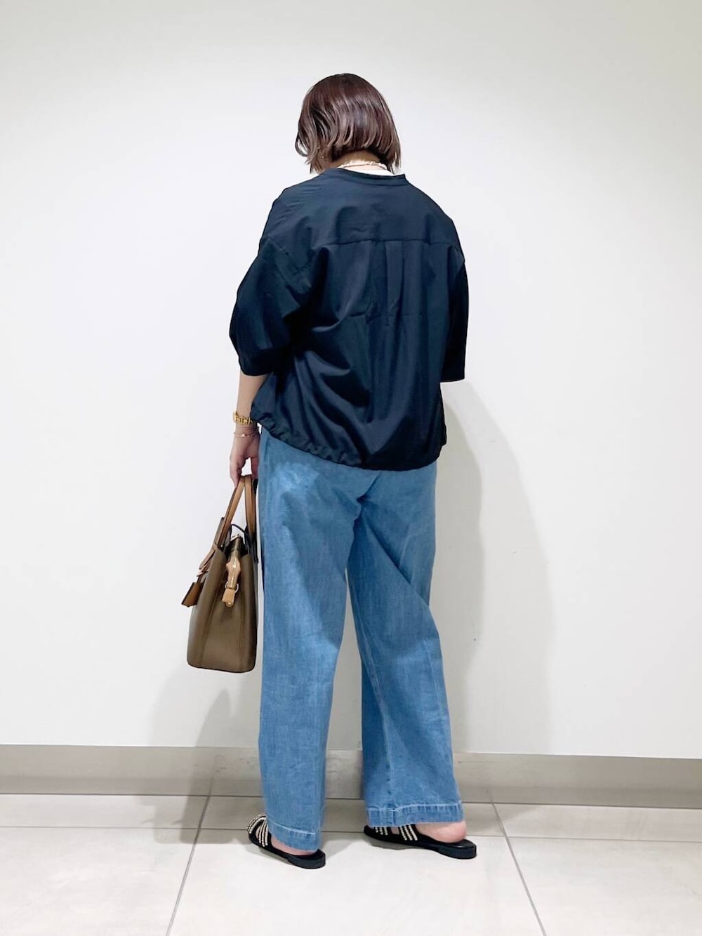 ブラウン系のトートバッグ、ブルー系のデニムパンツ、ブラック系のサンダルを着用したレディースの春コーディネートの5枚目の写真