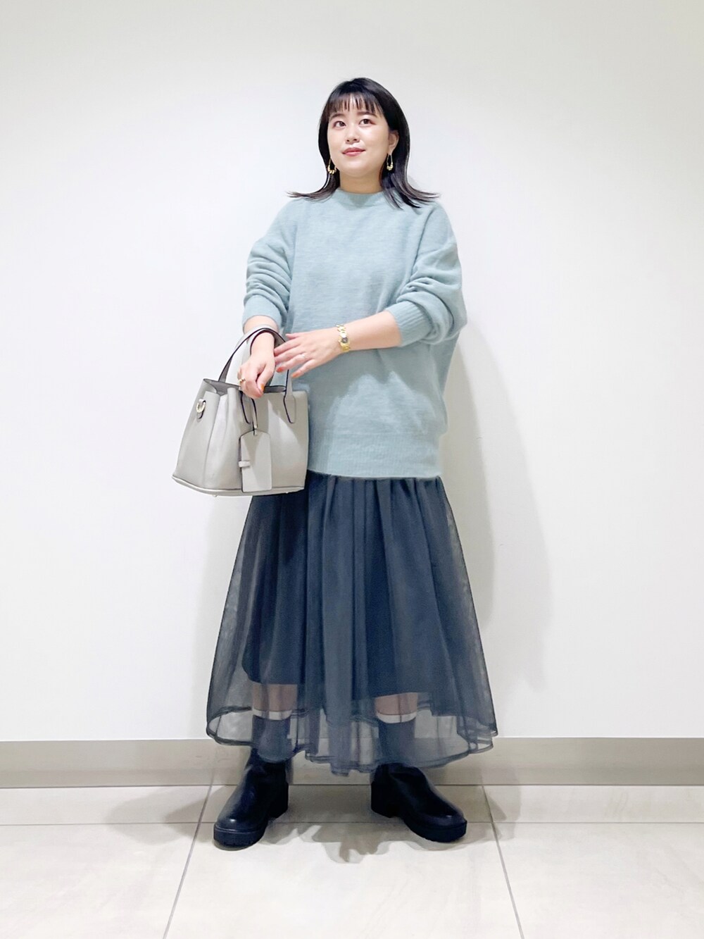 グリーン系のニット/セーター、グレー系のスカート、グレー系のトートバッグを着用したレディースの秋コーディネートの2枚目の写真
