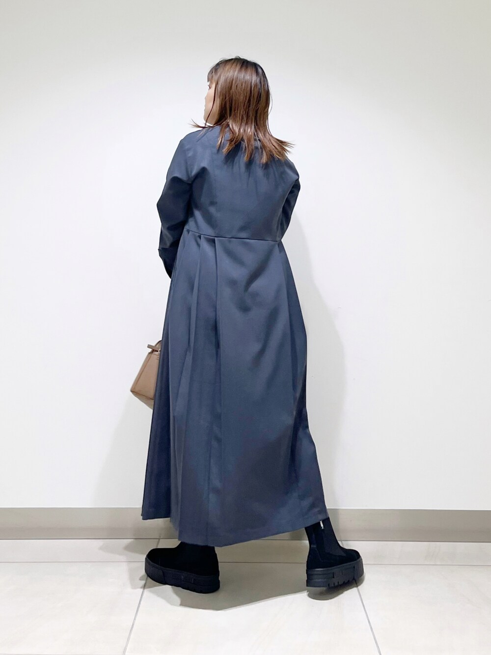 グレー系のワンピース、ブラウン系のショルダーバッグ、ブラック系のブーツを着用したレディースの秋コーディネートの4枚目の写真