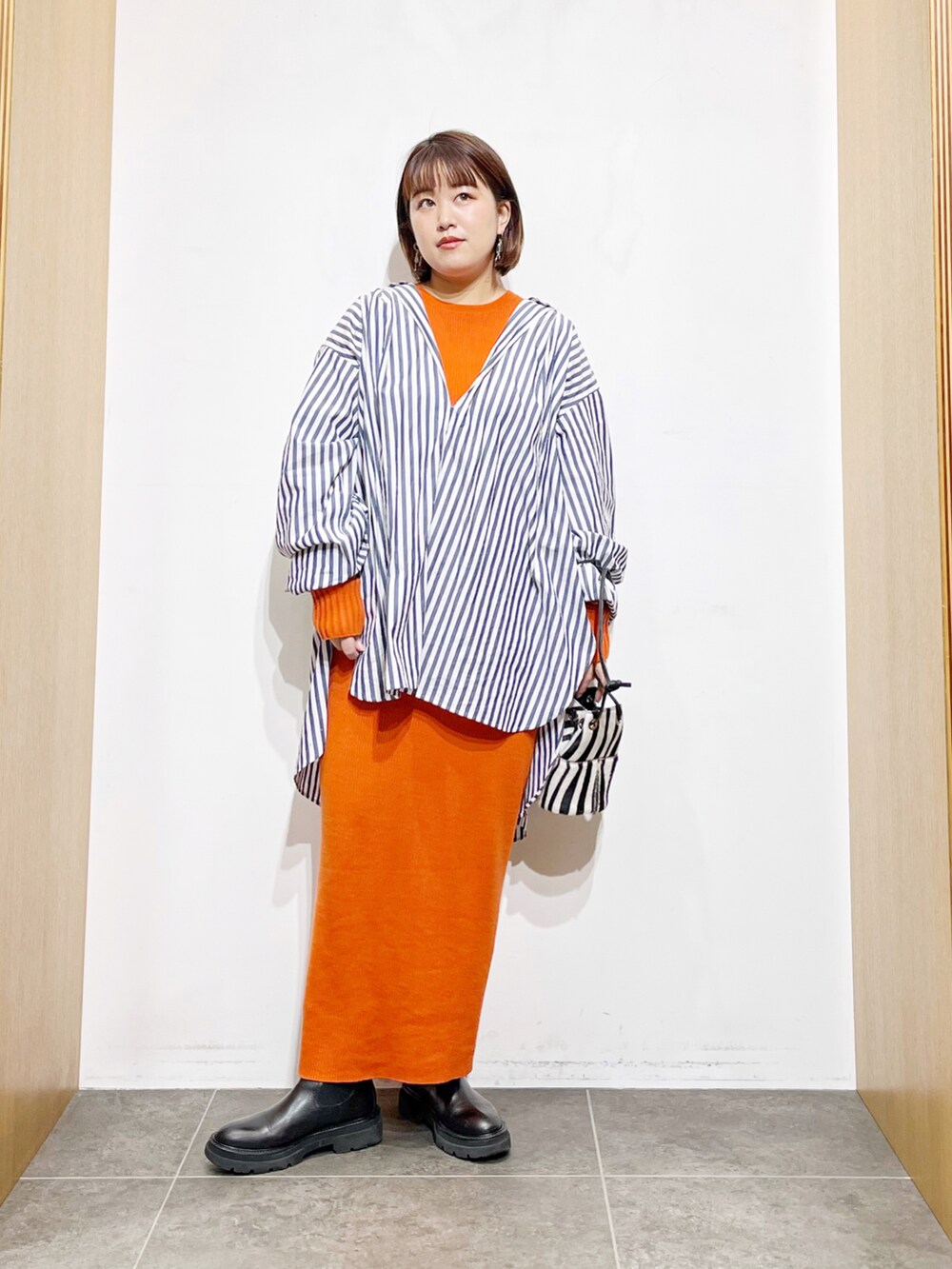 ブルー系のシャツ/ブラウス、オレンジ系のワンピース、ブラック系のブーツを着用したレディースの冬コーディネートの2枚目の写真