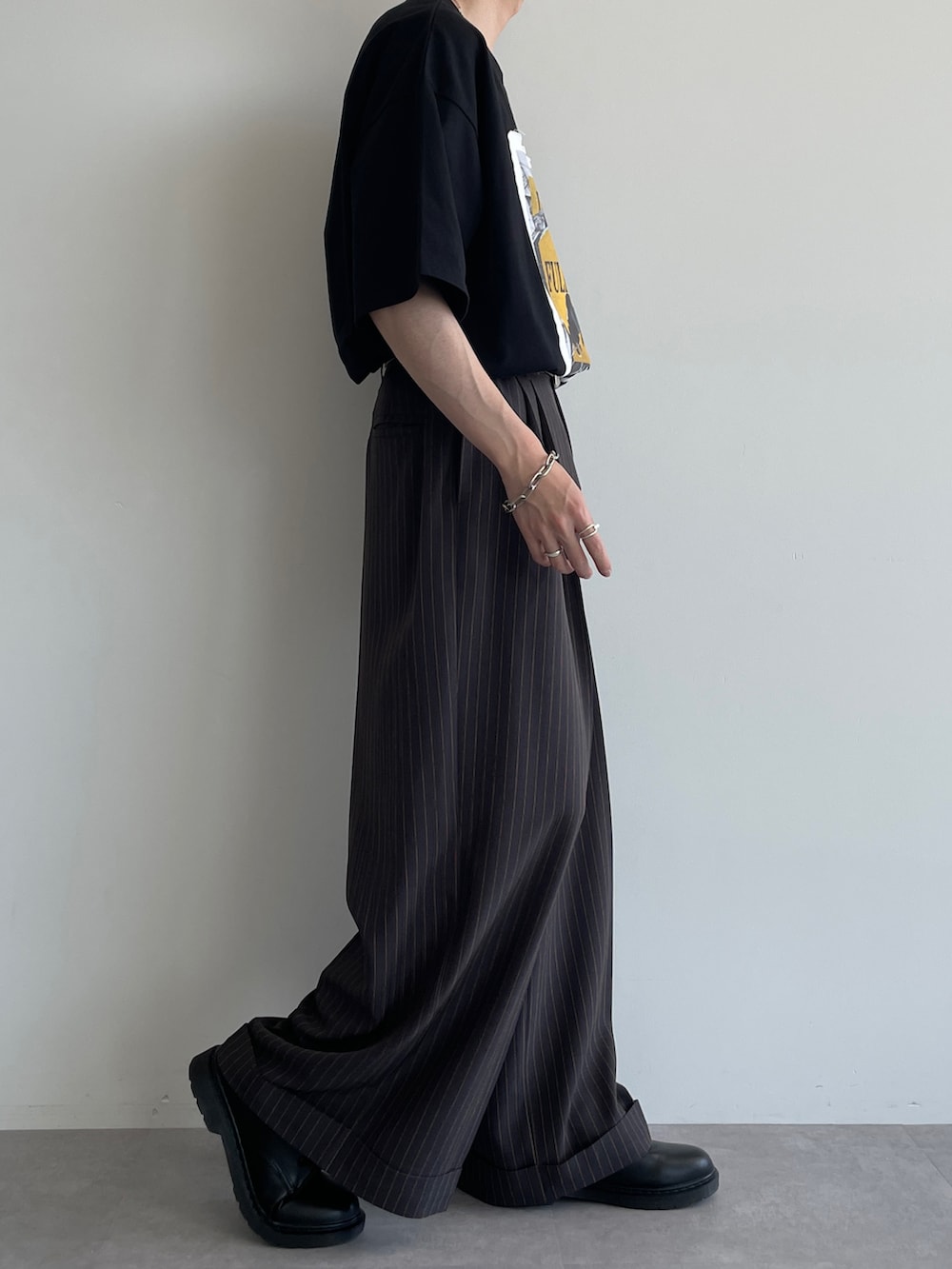 グレー系のスラックス、ブラック系のTシャツ/カットソー、ブラック系のシューズを着用したメンズの夏コーディネートの2枚目の写真