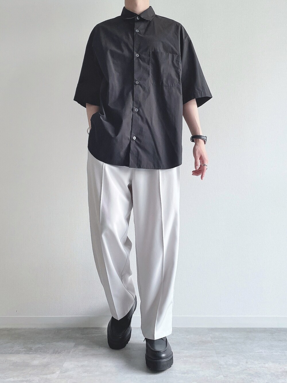 ブラック系のトップス、ホワイト系のスラックス、ブラック系のモカシン/デッキシューズを着用したメンズの夏コーディネートの2枚目の写真