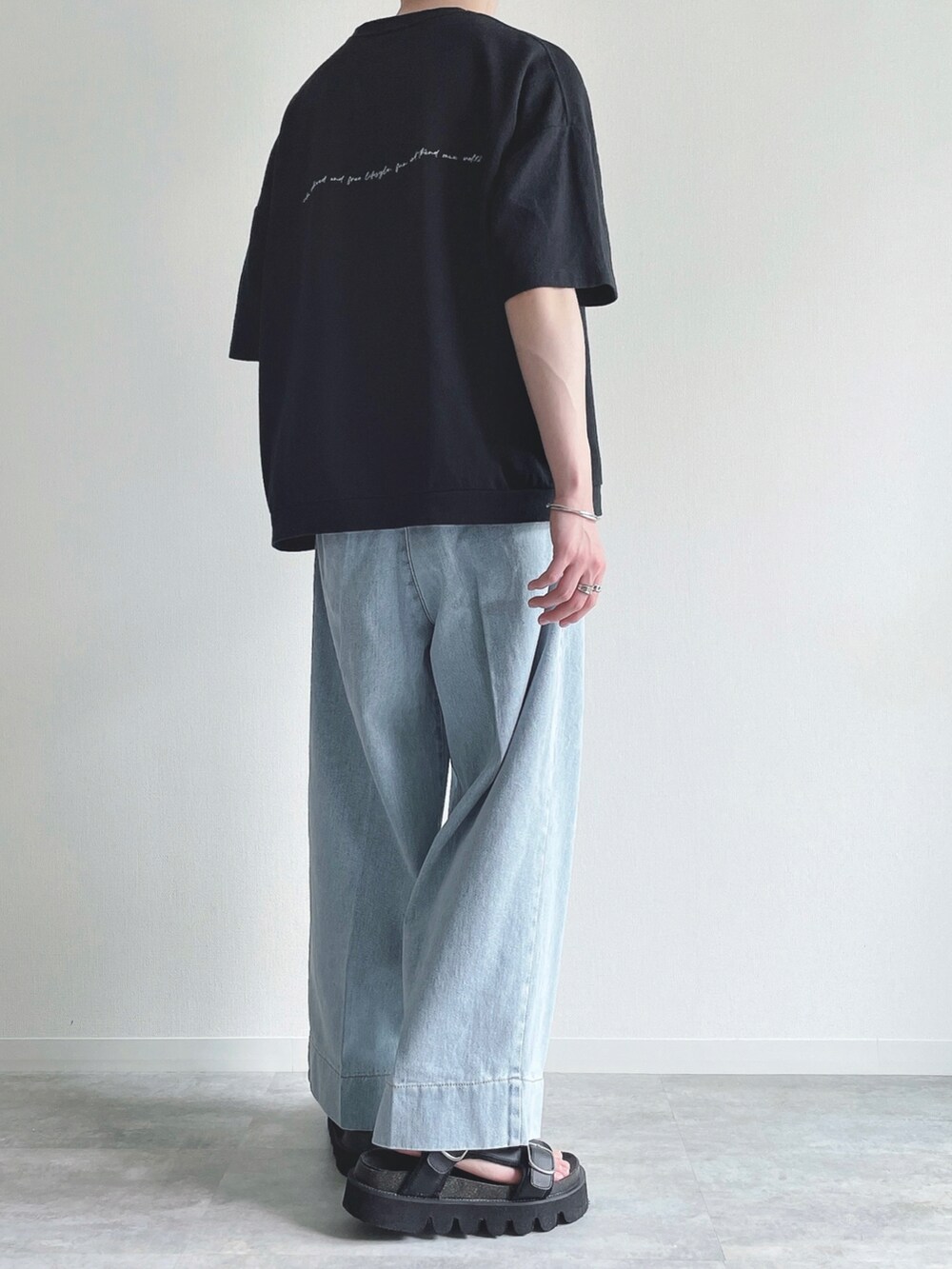 ブラック系のTシャツ/カットソー、ブルー系のデニムパンツ、ブラック系のサンダルを着用したメンズの夏コーディネートの3枚目の写真