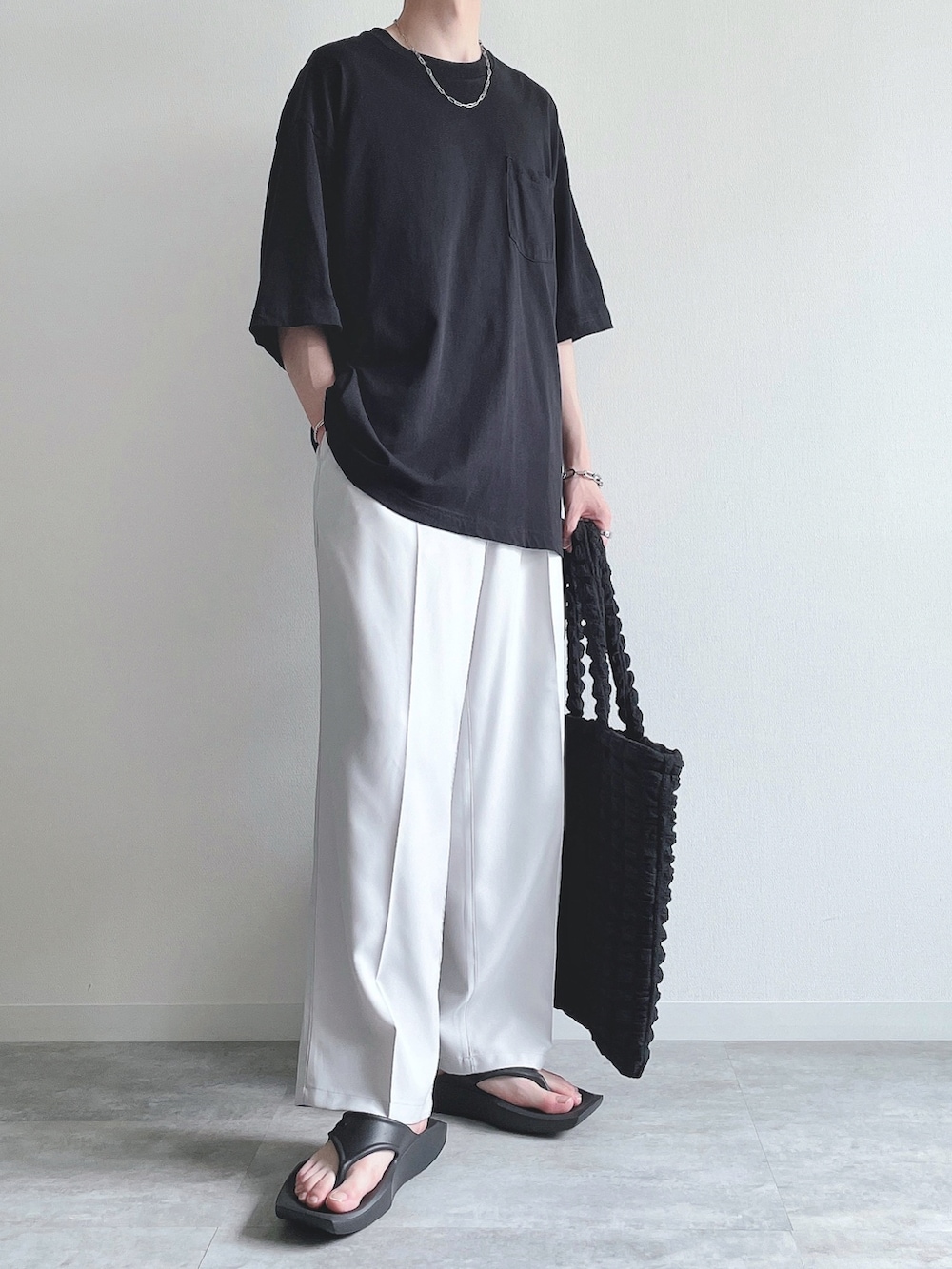 ブラック系のトップス、ホワイト系のスラックス、ブラック系のサンダルを着用したメンズの夏コーディネートの2枚目の写真