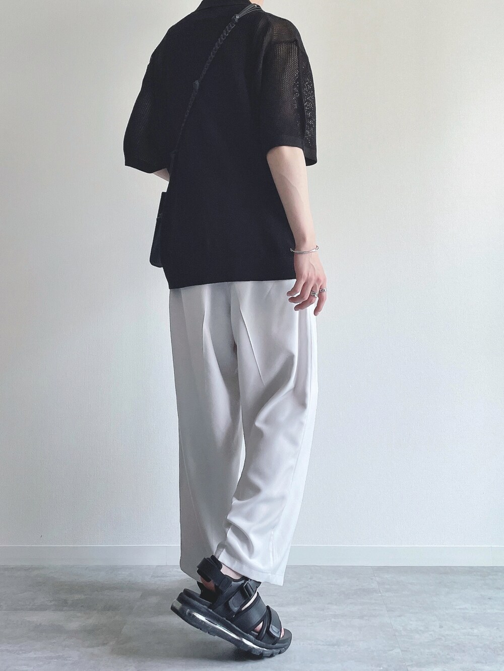 ブラック系のトップス、ホワイト系のスラックス、ブラック系のサンダルを着用したメンズの夏コーディネートの4枚目の写真