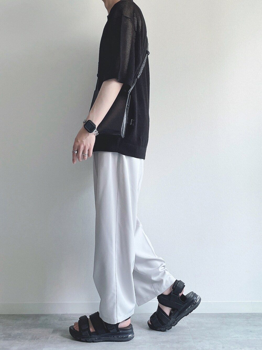 ブラック系のトップス、ホワイト系のスラックス、ブラック系のサンダルを着用したメンズの夏コーディネートの3枚目の写真