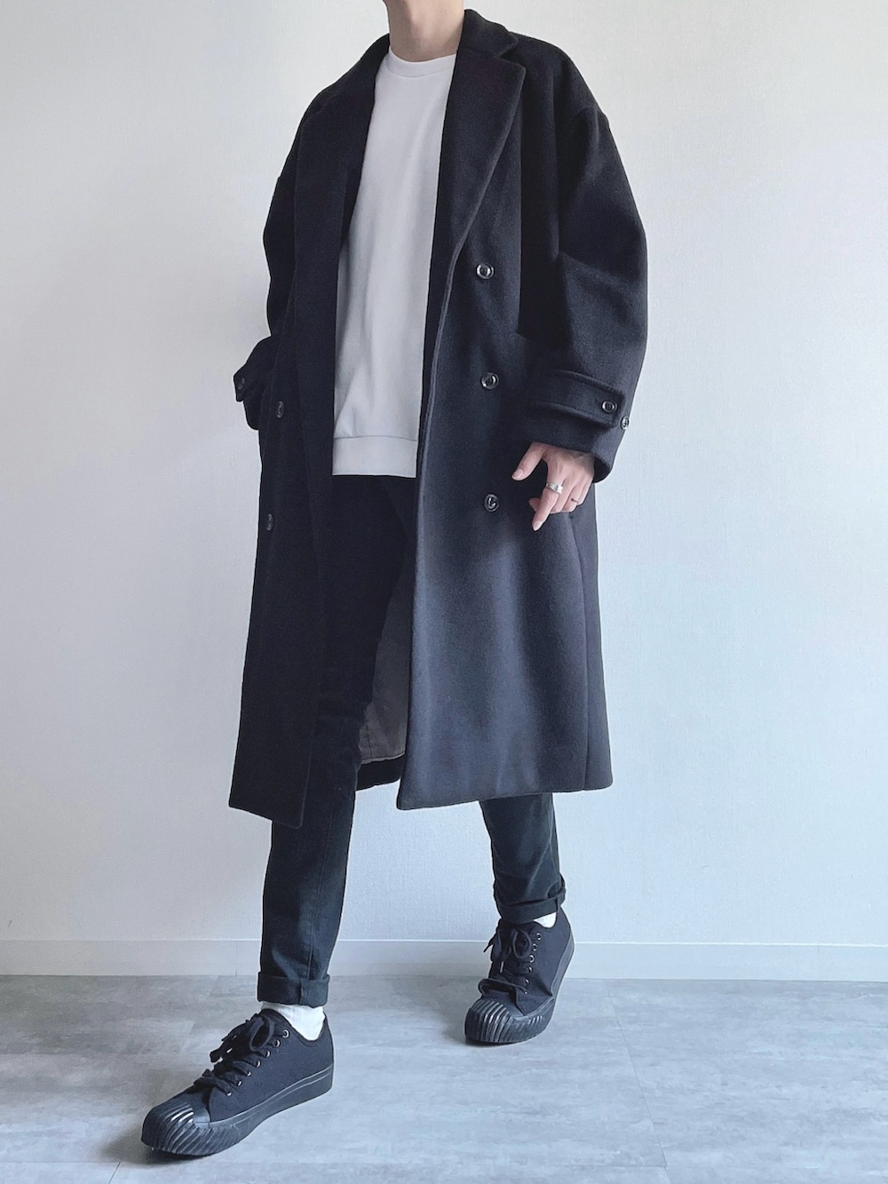 ブラック系のチェスターコート、ホワイト系のトップス、ブラック系のパンツを着用したメンズの冬コーディネートの5枚目の写真