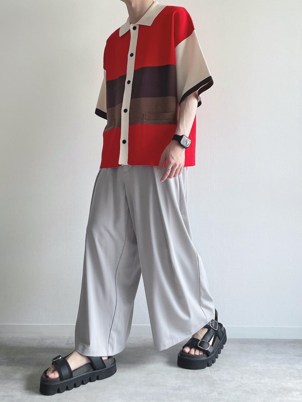 レッド系のポロシャツ、グレー系のスラックス、ブラック系のサンダルを着用したメンズの夏コーディネートの5枚目の写真