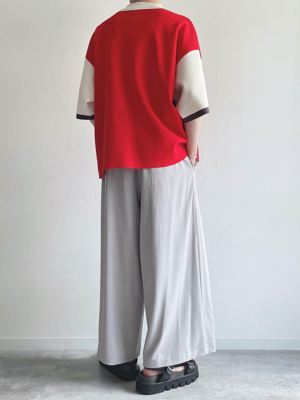 レッド系のポロシャツ、グレー系のスラックス、ブラック系のサンダルを着用したメンズの夏コーディネートの4枚目の写真