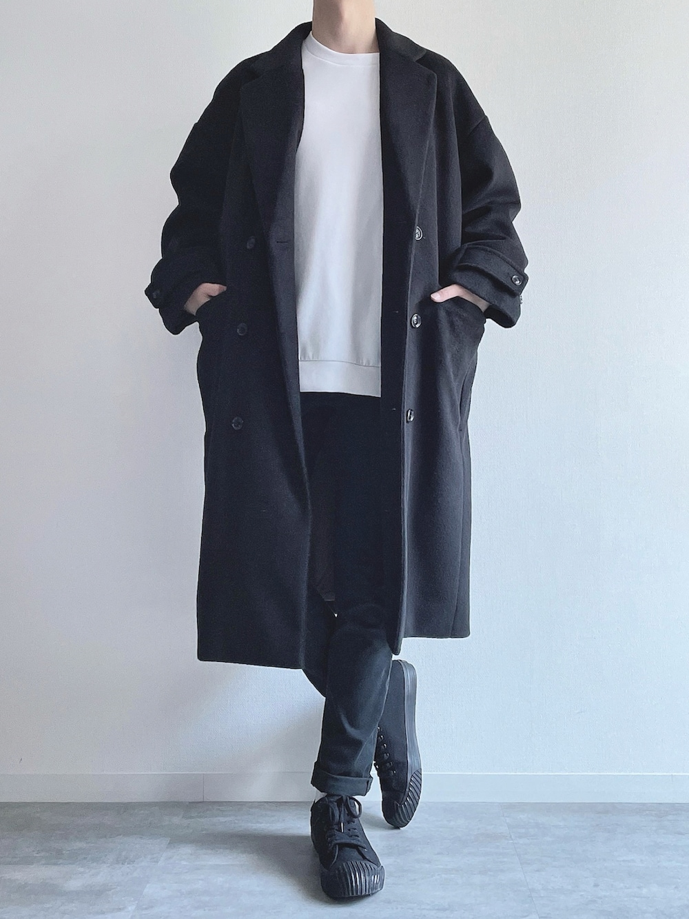 ブラック系のチェスターコート、ホワイト系のトップス、ブラック系のパンツを着用したメンズの冬コーディネートの4枚目の写真