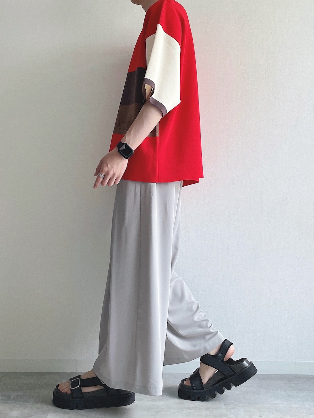 レッド系のポロシャツ、グレー系のスラックス、ブラック系のサンダルを着用したメンズの夏コーディネートの3枚目の写真