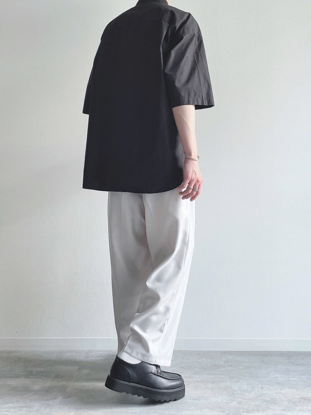 ブラック系のトップス、ホワイト系のスラックス、ブラック系のモカシン/デッキシューズを着用したメンズの夏コーディネートの3枚目の写真