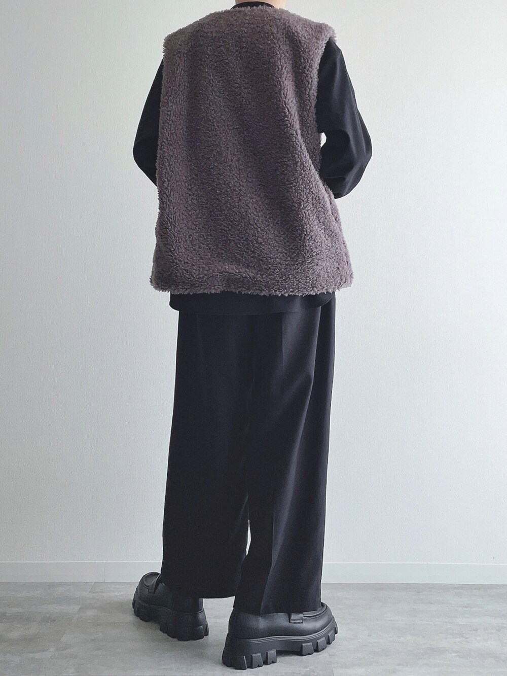 グレー系のベスト、ブラック系のトップス、ブラック系のスラックスを着用したメンズの秋コーディネートの3枚目の写真