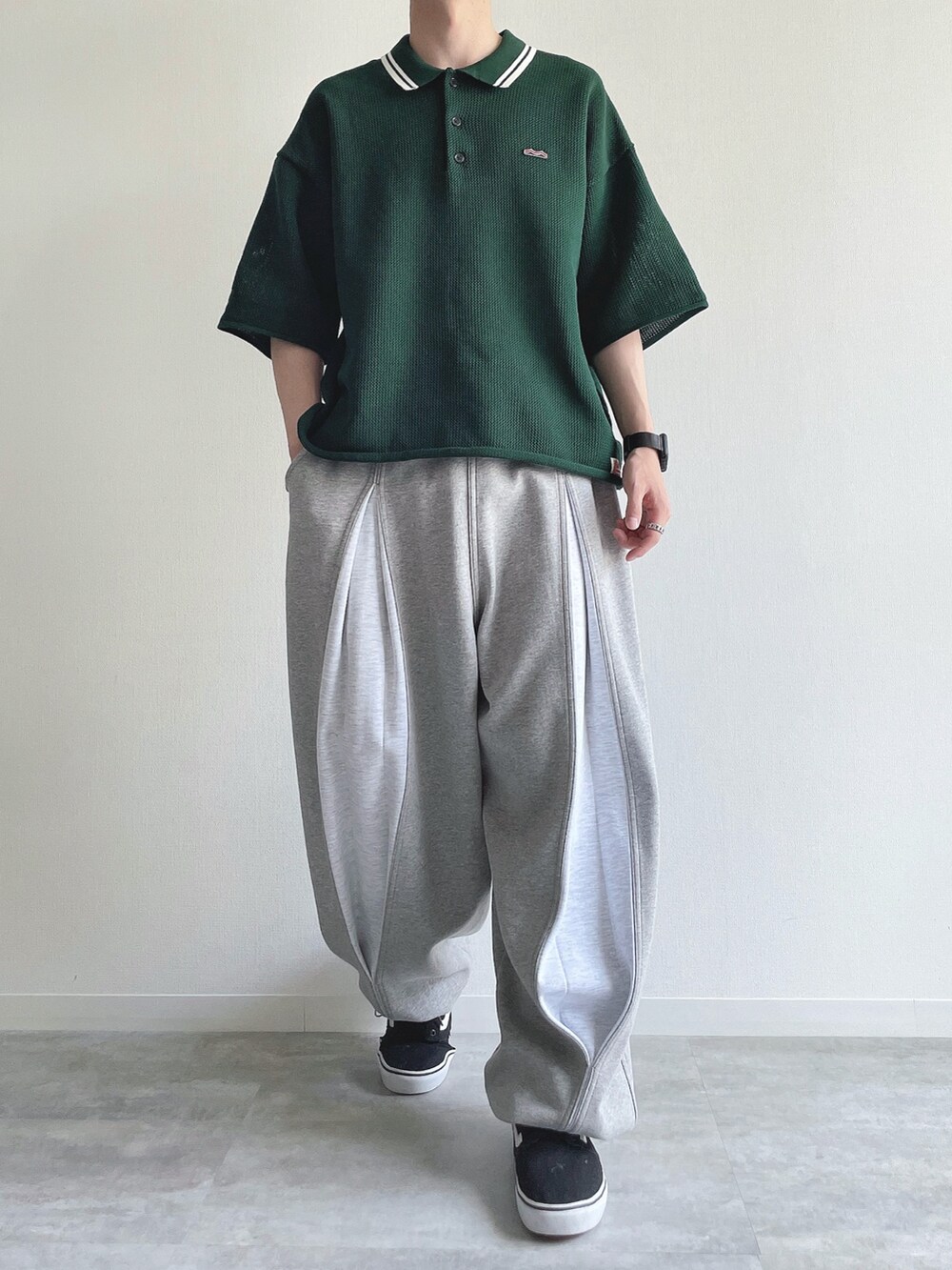 グリーン系のポロシャツ、グレー系のパンツ、ブラック系のスニーカーを着用したメンズの夏コーディネートの2枚目の写真