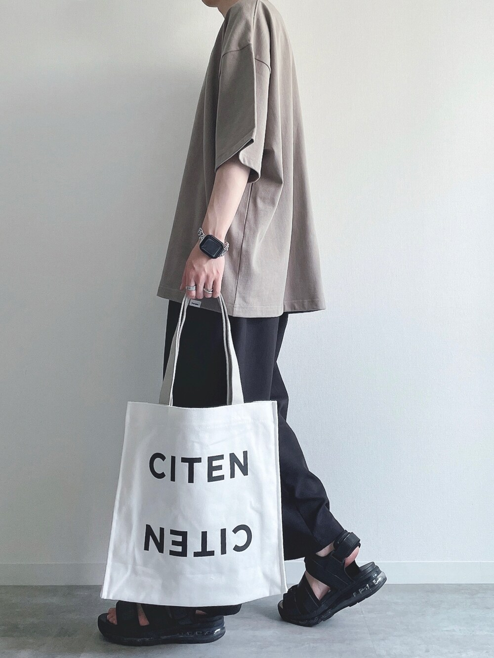 ベージュ系のTシャツ/カットソー、ブラック系のスラックス、ブラック系のサンダルを着用したメンズの夏コーディネートの3枚目の写真