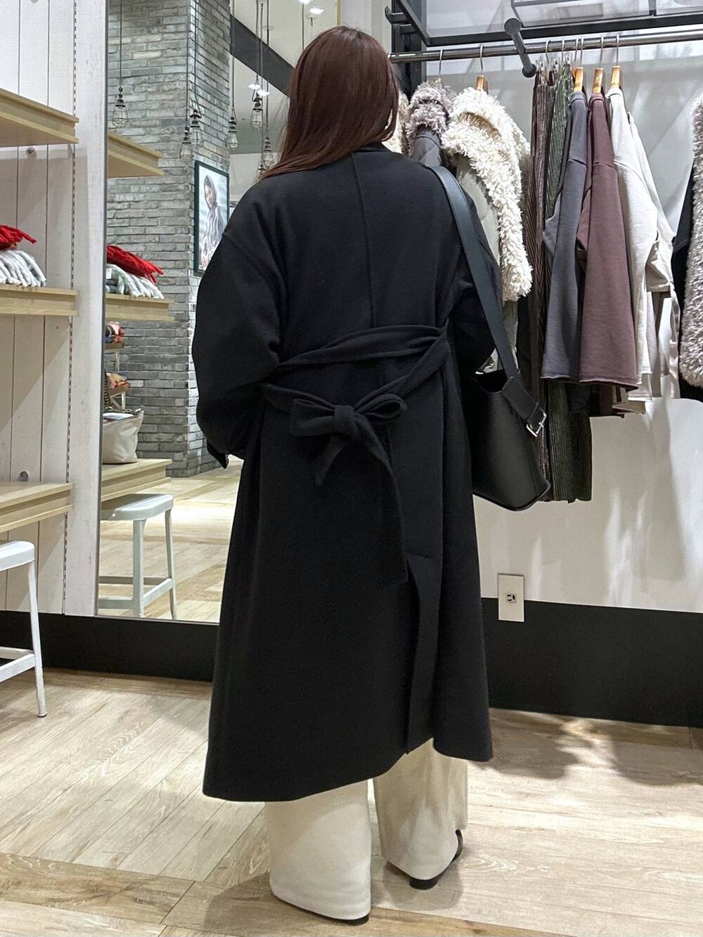 ブラック系のステンカラーコート、ブラック系のショルダーバッグ、ブラック系のブーツを着用したレディースの冬コーディネートの3枚目の写真