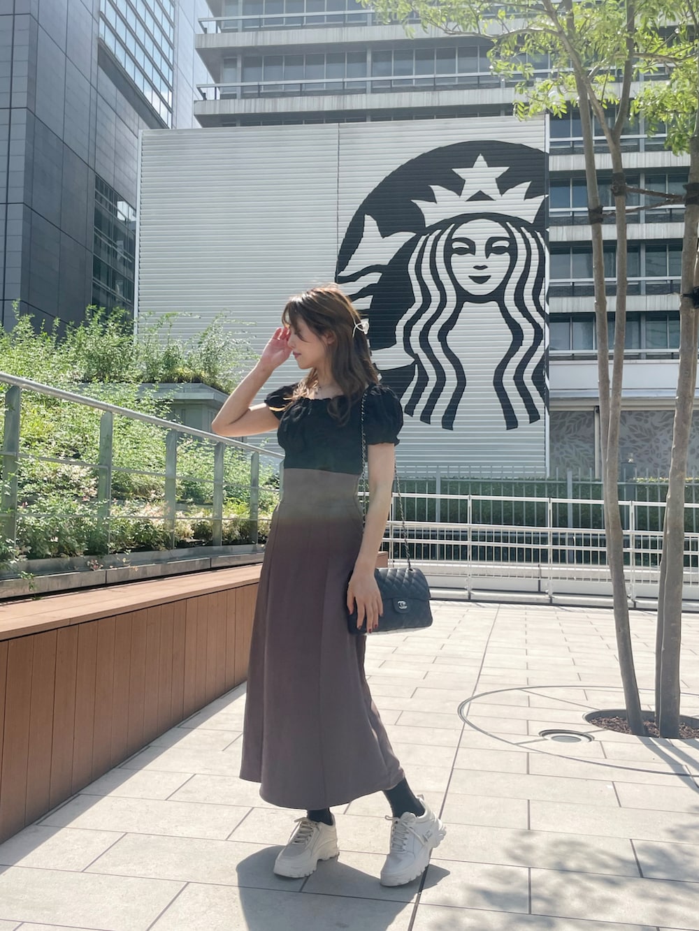 ブラウン系のスカート、ブラック系のトップス、ホワイト系のスニーカーを着用したレディースの秋コーディネートの2枚目の写真