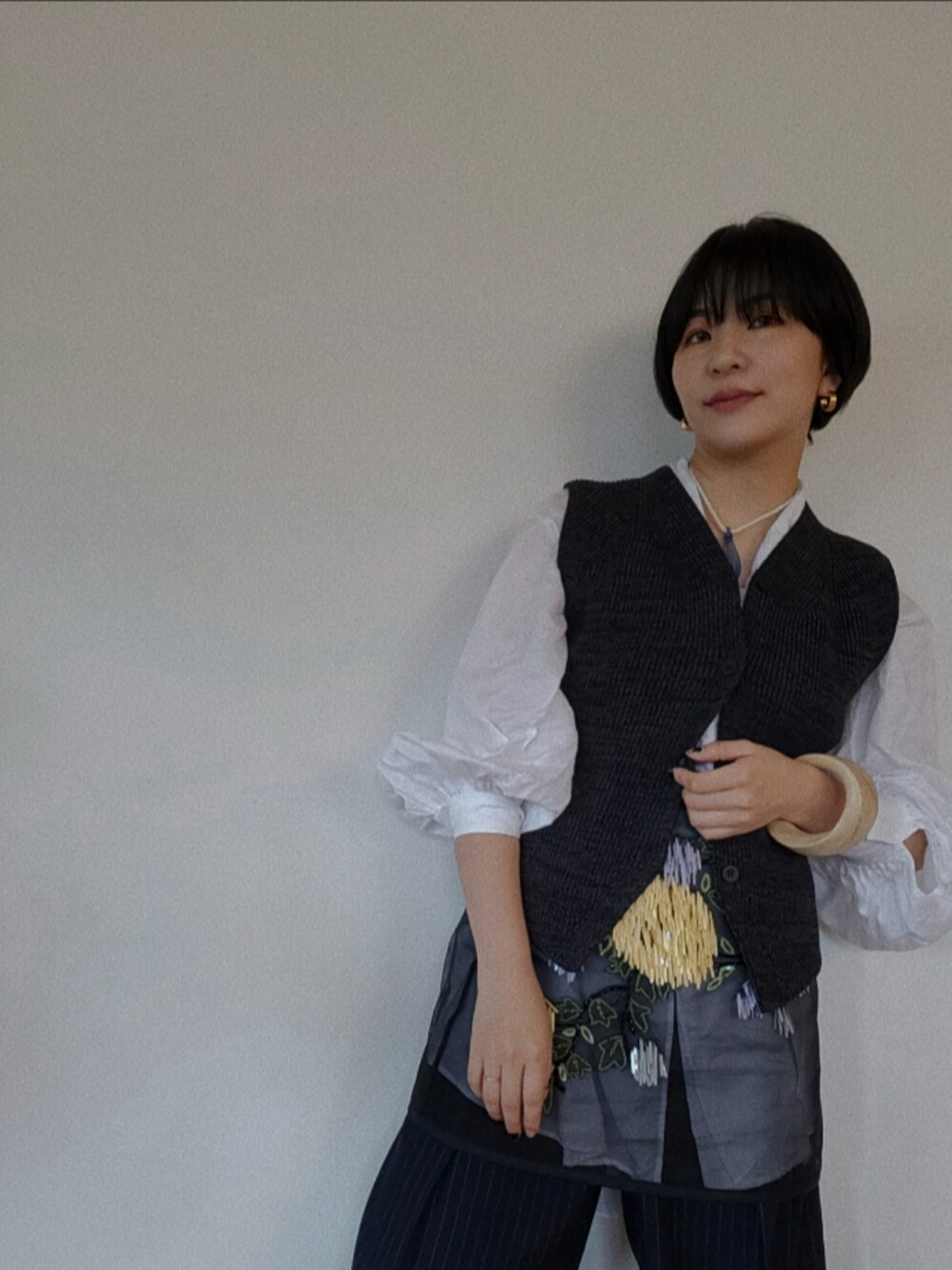 ブラック系のスカート、グレー系のベスト、ベージュ系のブレスレットを着用したレディースの春コーディネートの2枚目の写真