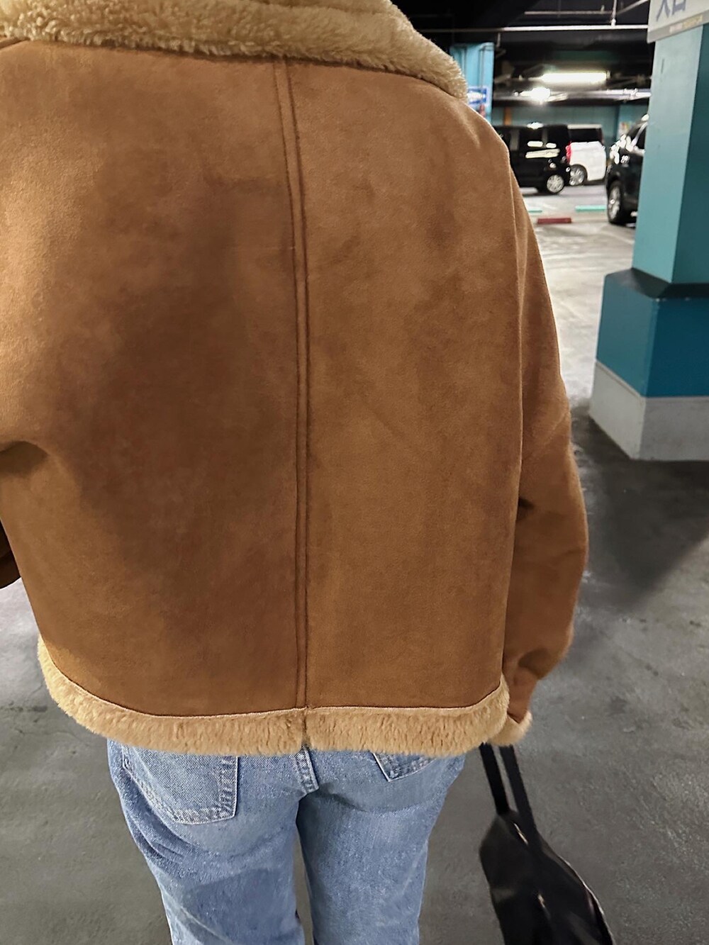 ブラウン系のムートンコート、ブルー系のデニムパンツ、ブラック系のハンドバッグを着用したレディースの冬コーディネートの5枚目の写真