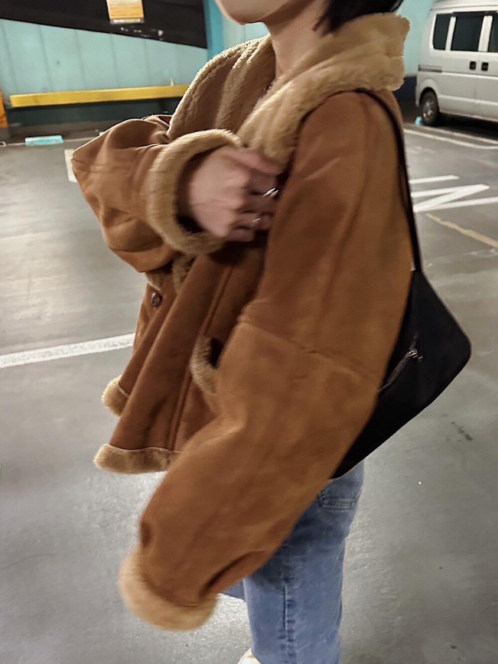 ブラウン系のムートンコート、ブルー系のデニムパンツ、ブラック系のハンドバッグを着用したレディースの冬コーディネートの4枚目の写真