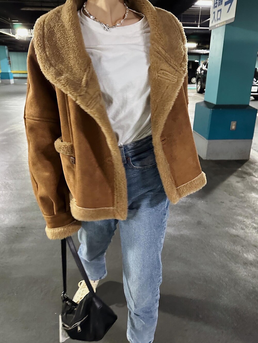 ブラウン系のムートンコート、ブルー系のデニムパンツ、ブラック系のハンドバッグを着用したレディースの冬コーディネートの3枚目の写真