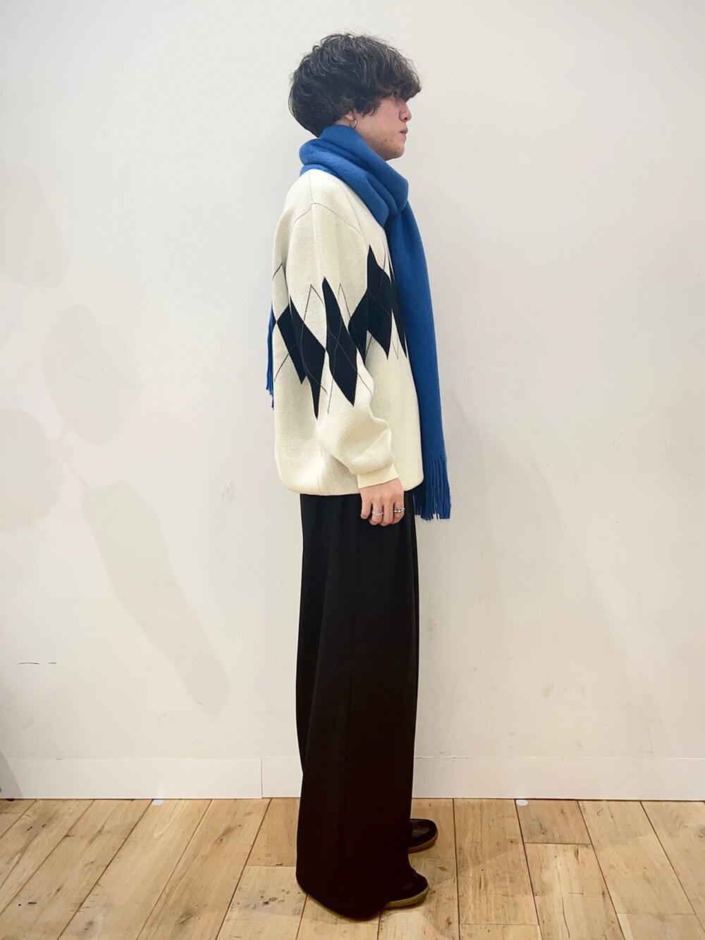 ホワイト系のニット/セーター、ブラック系のスラックス、ブルー系のストール/ショールを着用したメンズの冬コーディネートの2枚目の写真