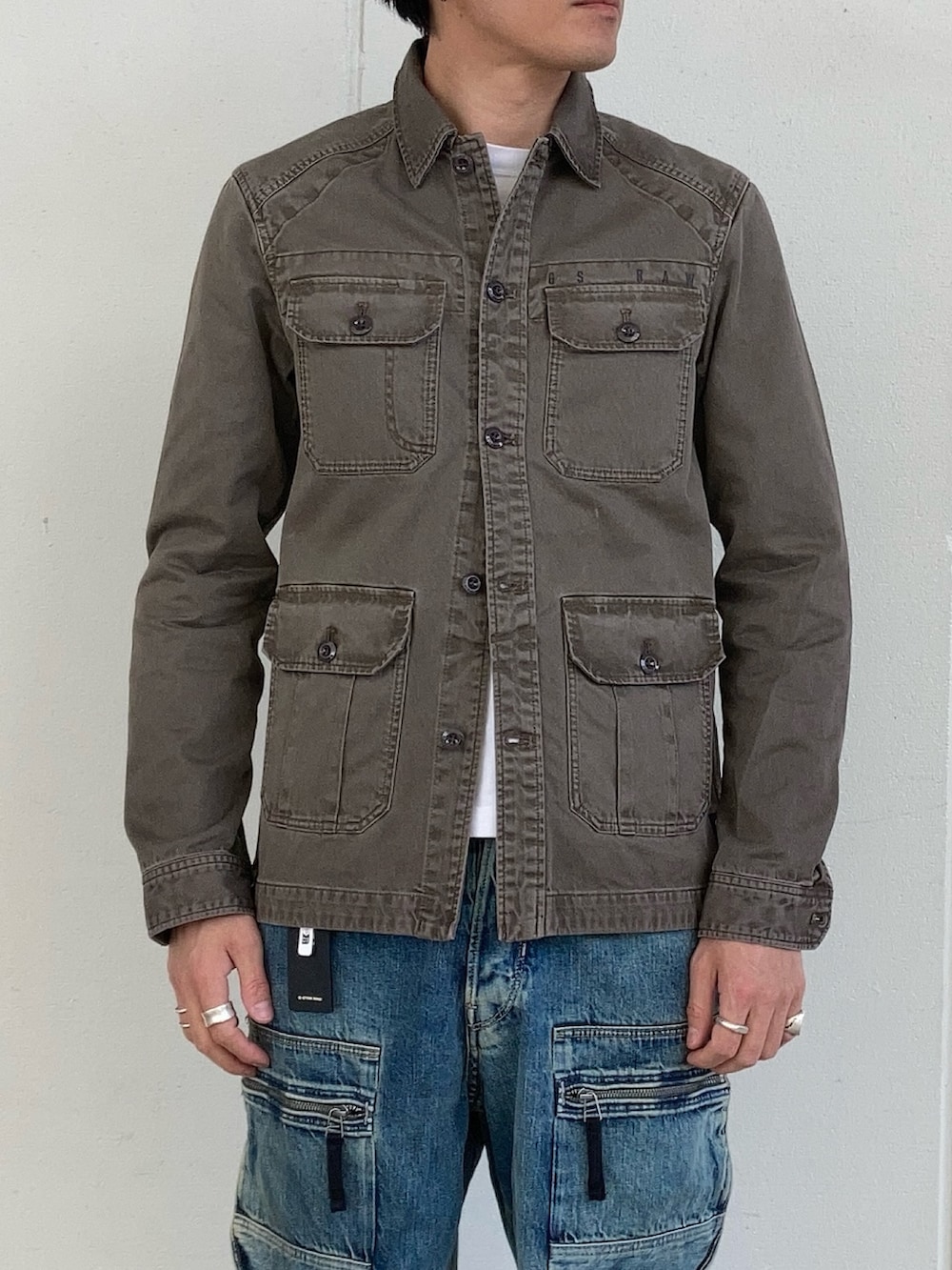 ベージュ系のミリタリージャケット、ブルー系のデニムパンツを着用したメンズの春コーディネートの2枚目の写真