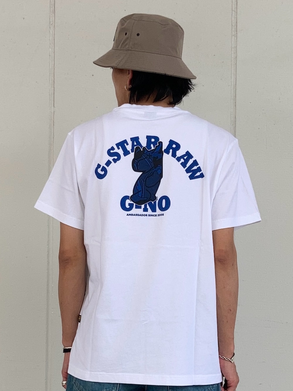 ホワイト系のTシャツ/カットソー、ブルー系のデニムパンツ、ベージュ系の帽子を着用したメンズの夏コーディネートの2枚目の写真