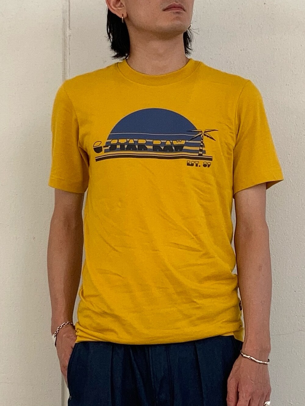 イエロー系のTシャツ/カットソー、ブルー系のデニムパンツ、ブルー系のキャップを着用したメンズの夏コーディネートの2枚目の写真