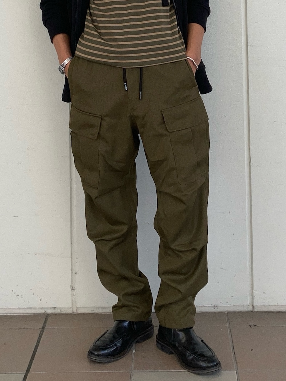 ブラック系のパーカー、グリーン系のTシャツ/カットソー、グリーン系のカーゴパンツを着用したメンズの秋コーディネートの2枚目の写真