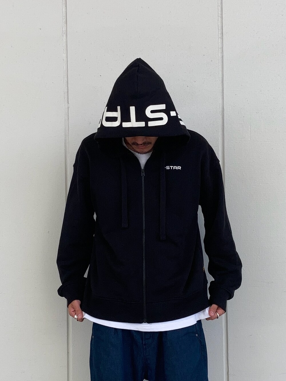 ブラック系のパーカー、ホワイト系のTシャツ/カットソー、ブルー系のデニムパンツを着用したメンズの秋コーディネートの2枚目の写真