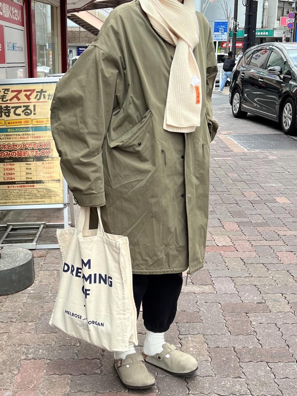グリーン系のモッズコート、ホワイト系のトートバッグ、ベージュ系のサンダルを着用したレディースの冬コーディネートの2枚目の写真