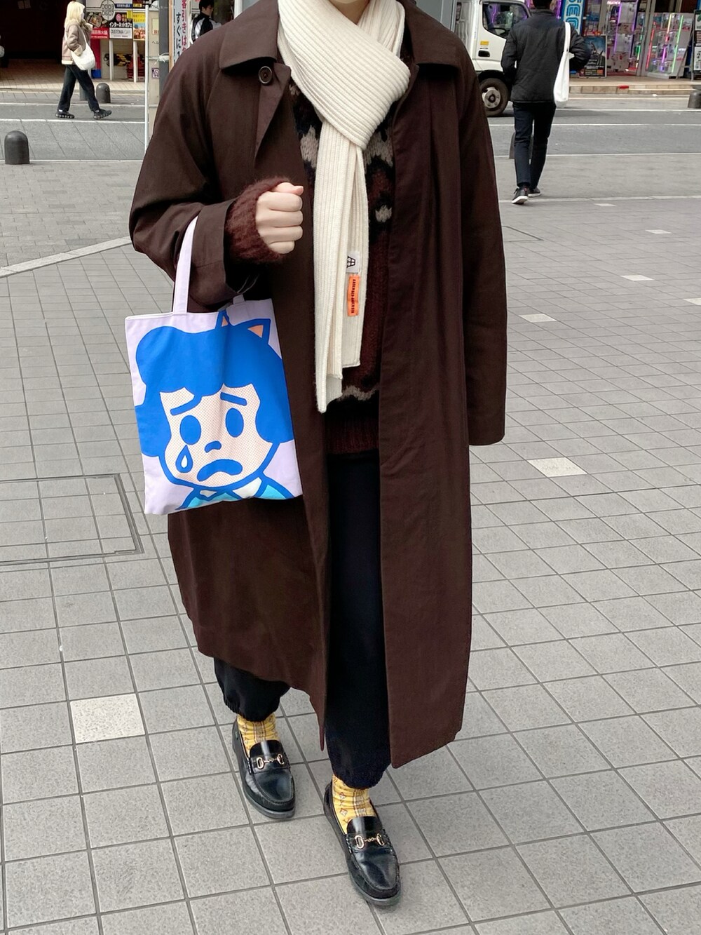 ブラウン系のステンカラーコート、ブラウン系のニット/セーター、ブラック系のローファーを着用したレディースの冬コーディネートの2枚目の写真