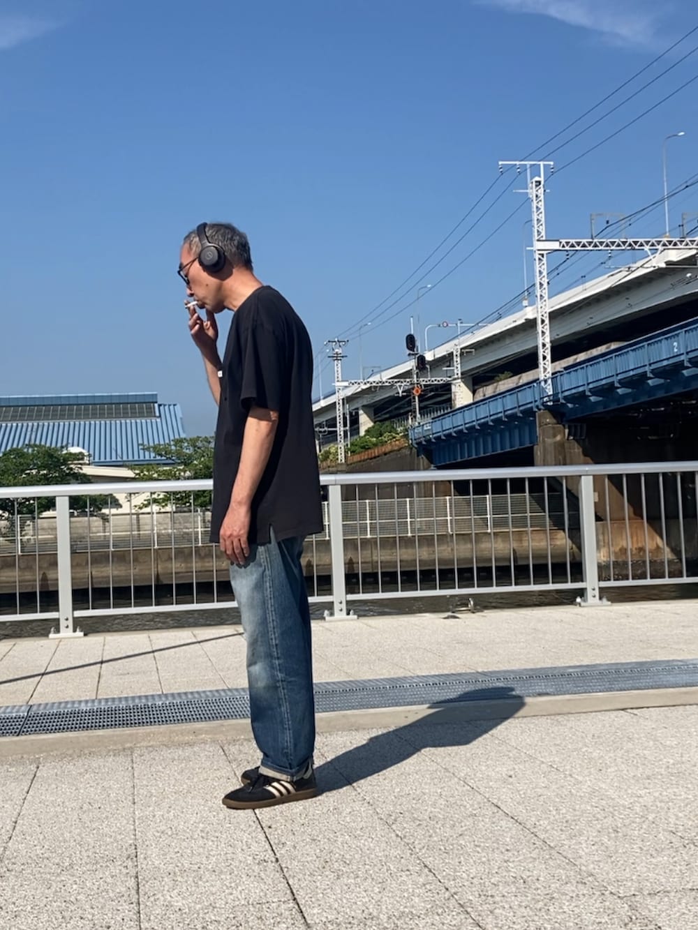 ブルー系のデニムパンツ、ブラック系のTシャツ/カットソー、ブラック系のスニーカーを着用したメンズの夏コーディネートの2枚目の写真