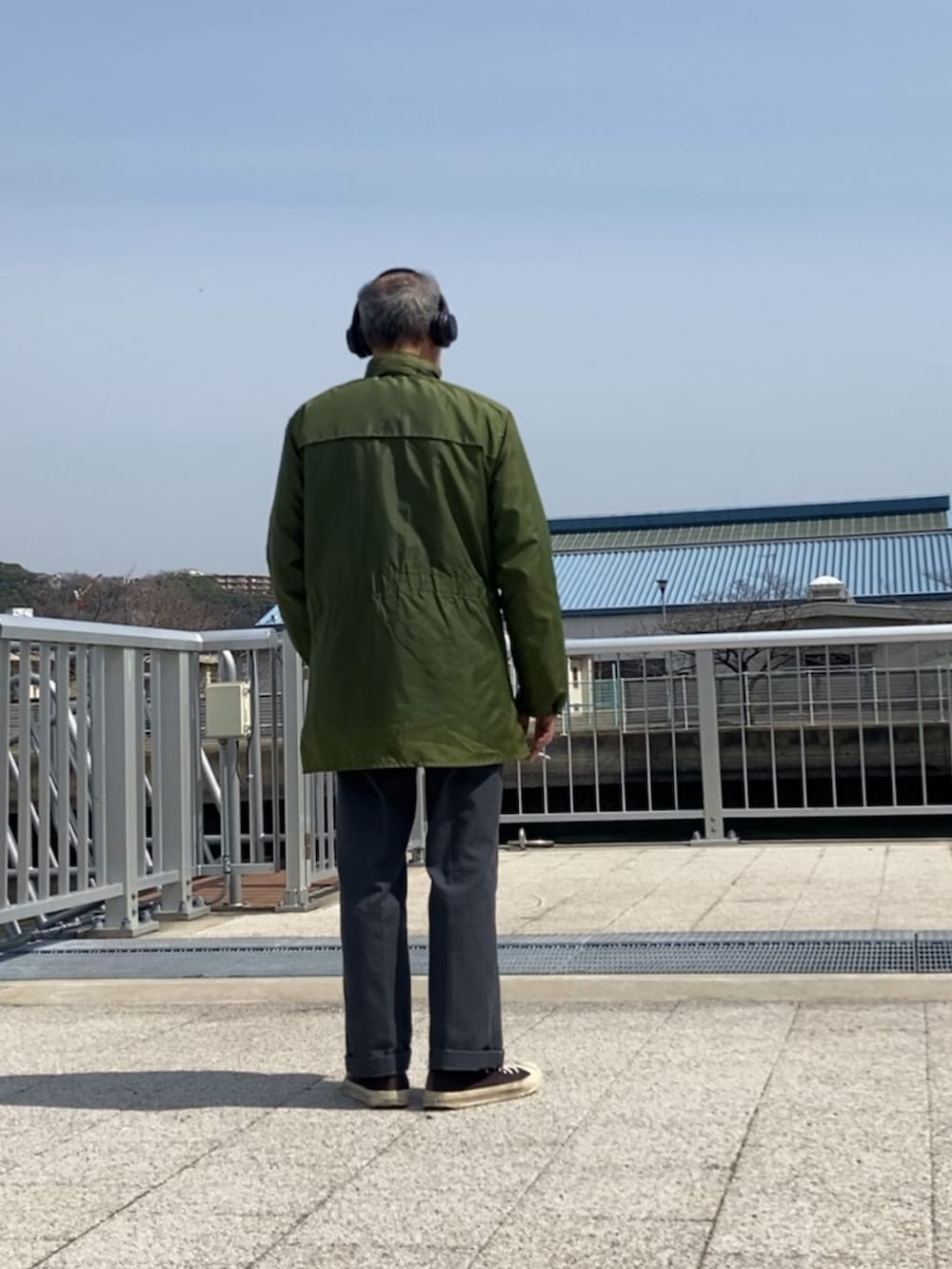 グリーン系のミリタリージャケット、グレー系のチノパンツ、ブラック系のスニーカーを着用したメンズの春コーディネートの3枚目の写真