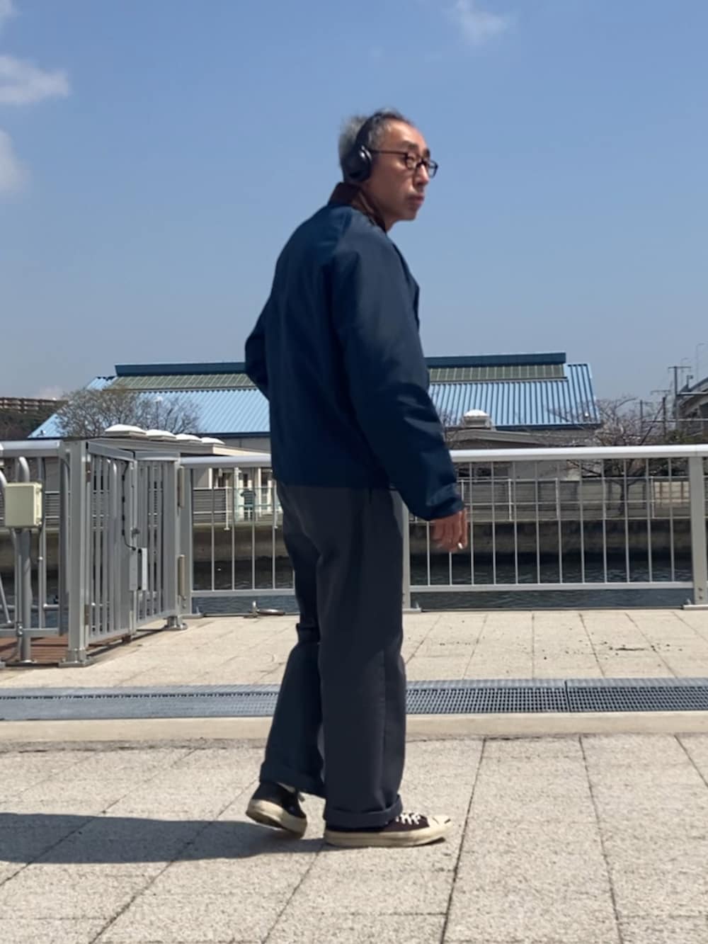 ブルー系のナイロンジャケット、グレー系のチノパンツ、ブラック系のスニーカーを着用したメンズの春コーディネートの2枚目の写真